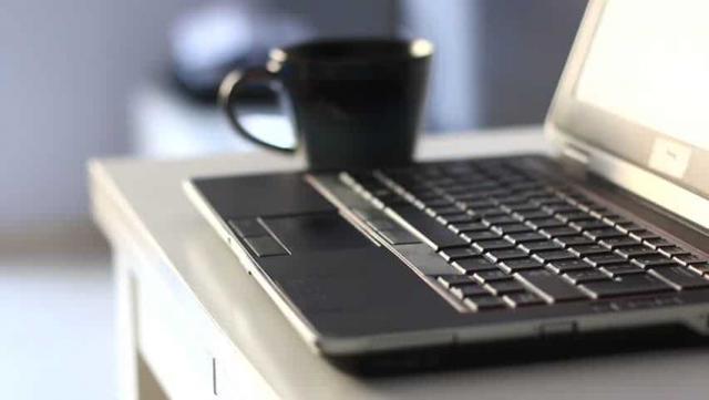 Un portátil sobre unha mesa cunha taza ao carón.